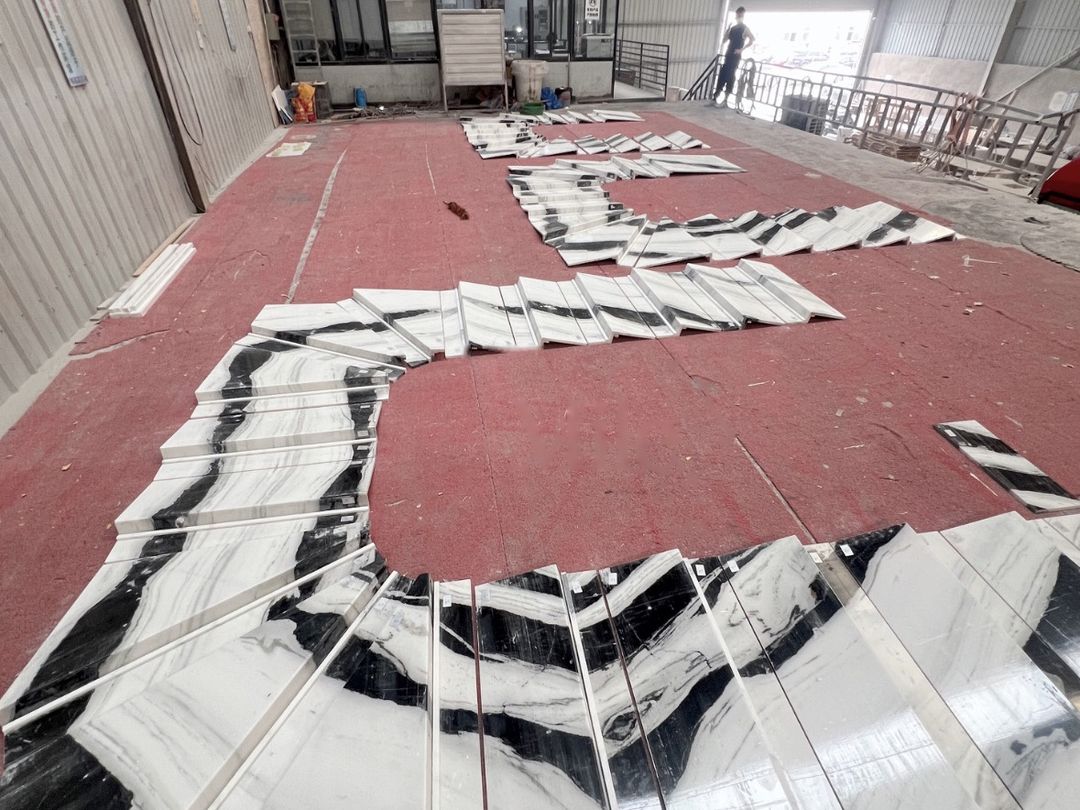 Custom curved stair treads in Panda White marble laid out in sequence on the factory floor